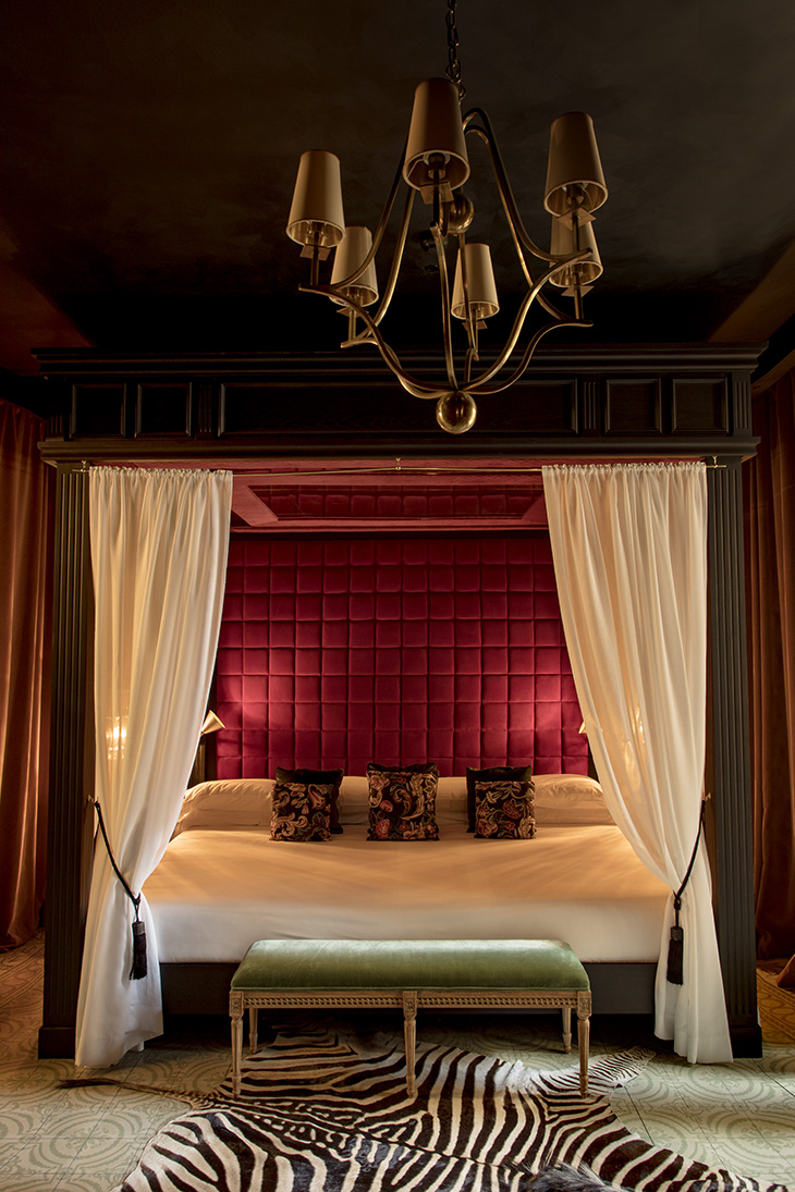 Cama con dosel, tapizado en terciopelo rojo y alfombra de cebra en la master suite del Hotel Palma Riad by Pablo Peyra Studio.