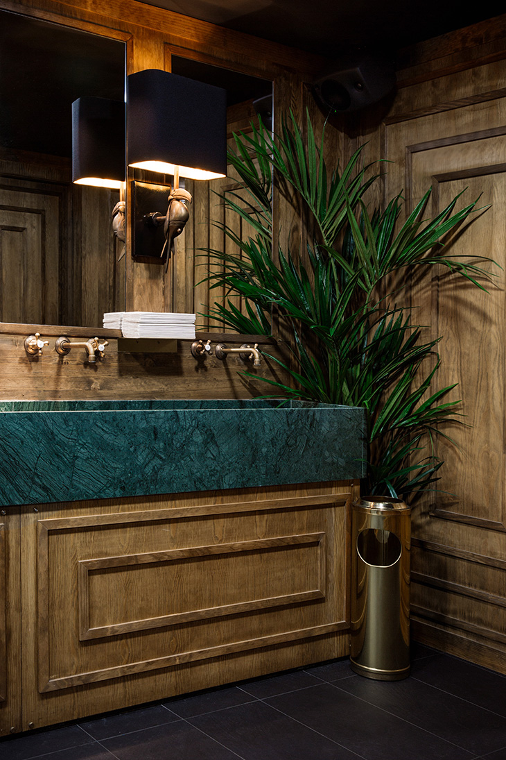 Interiorismo de restaurante por Pablo Peyra Studio. Proyecto Feroz, Barcelona. Baño de diseño elegante con lavamanos de mármol verde, paneles de madera, iluminación decorativa y planta ornamental. Interiorismo de restaurante por Pablo Peyra Studio. Proyecto Feroz, Barcelona. Baño de diseño elegante con lavamanos de mármol verde, paneles de madera, iluminación decorativa y planta ornamental.